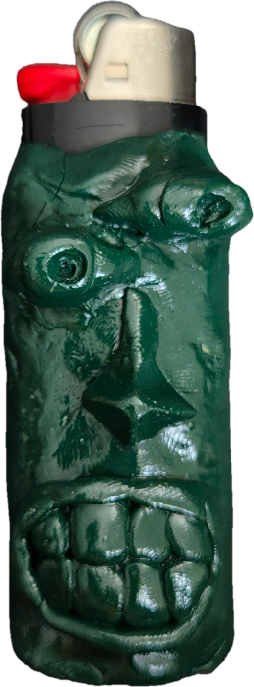 Monochrome, dunkelgrün glänzende Feuerzeughülle aus Knete. Das reliefartige, gruselige Gesicht hat asymmetrische, tief liegende Augen, eine spitze Nase und einen breit grinsenden Mund mit großen, quadratischen Zähnen.