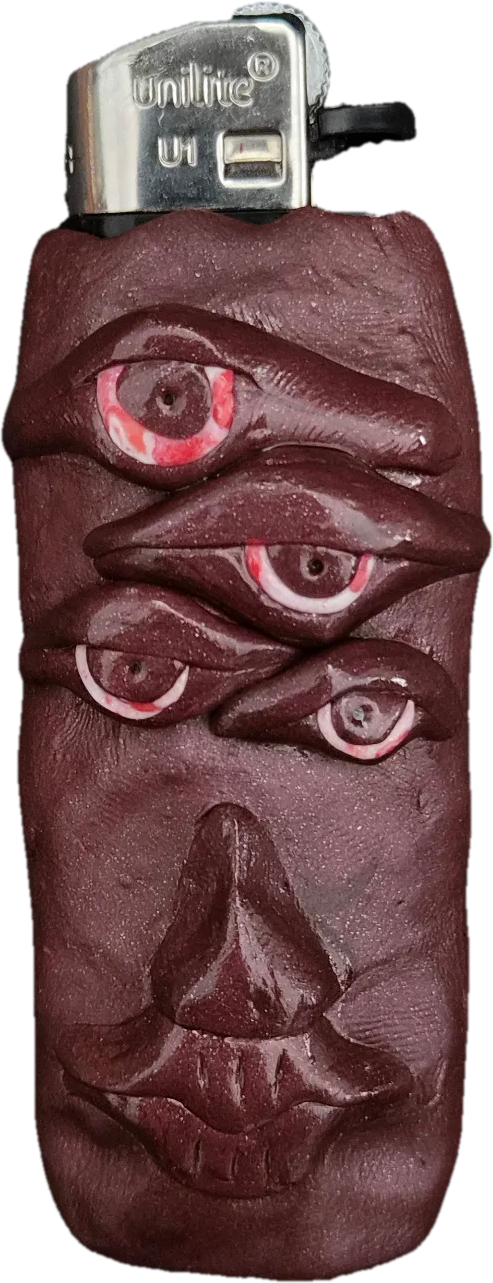 Dunkelbraune, strukturierte Feuerzeughülle aus Knete mit einem surrealen Motiv. Die obere Hälfte ist vertikal mit vier detailreichen Augen mit rot-weißen Pupillen besetzt, darunter befinden sich eine Nase und geschwungene Lippen.