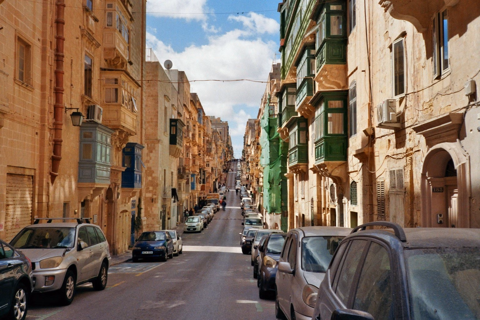 Schmale Gasse in Malta mit traditionellen, bunten Holzbalkonen und sandsteinfarbenen Häusern.