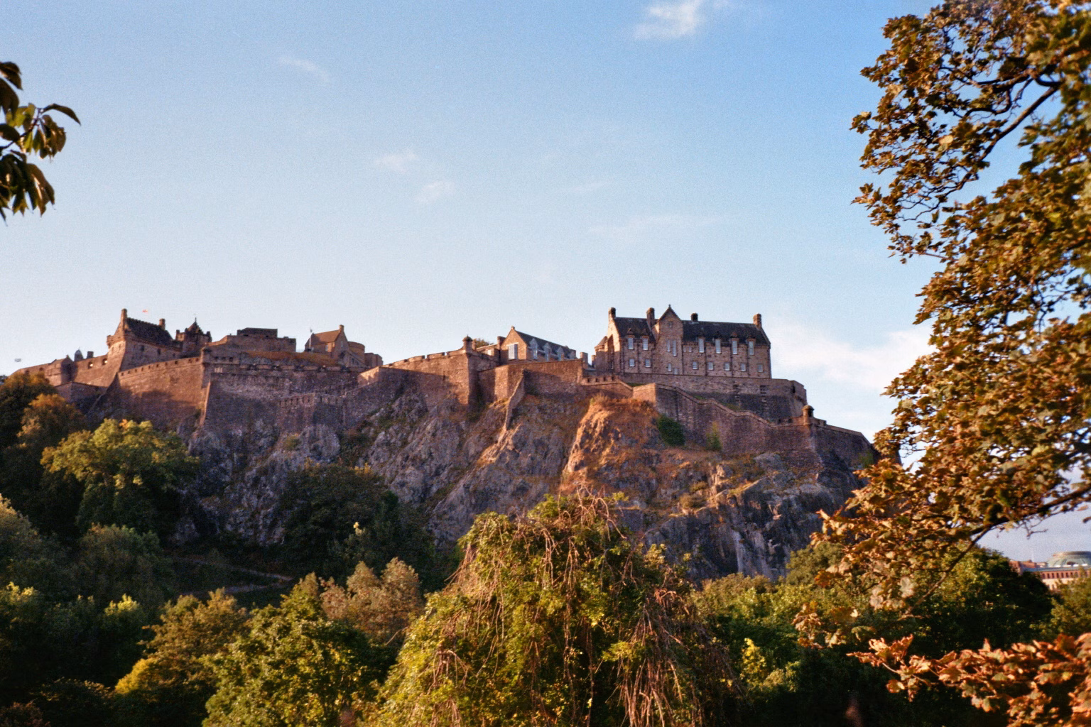 Das historische Edinburgh Castle auf einem steilen Felsen über grünen Baumkronen.