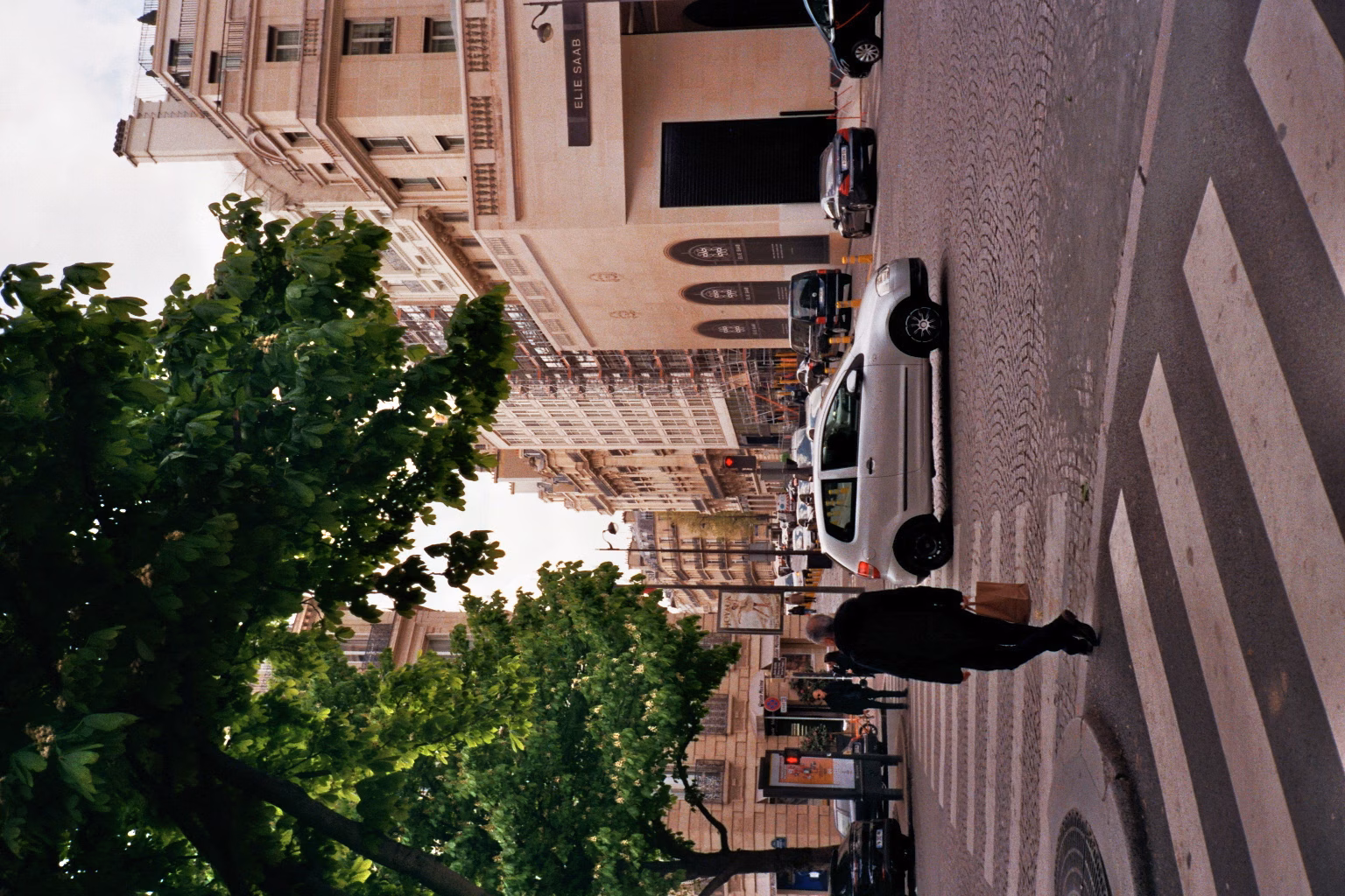 Analoge Straßenfotografie einer Pariser Kopfsteinpflaster-Kreuzung mit Passanten und Autos vor eleganten Stadthäusern.